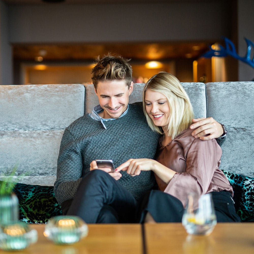 Una coppia utilizza la Guida digitale per gli ospiti di Hotelcore su uno smartphone nella hall dell’hotel